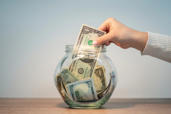 homeowner putting a dollar bill in a clear jar depicting Save on Heating Oil