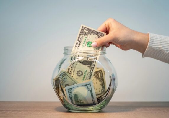 homeowner putting a dollar bill in a clear jar depicting Save on Heating Oil